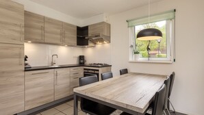 A modern kitchen with wooden cabinets, a gas stove, and a dining area with a table and chairs. - Detached bungalow for 8 persons (Eernewoude)