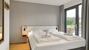 A modern hotel room with a large bed, two bedside tables, a wall-mounted lamp, and a view of a garden through a sliding glass door. - Comfortable bungalow for 6 persons at the waterfront (Midlaren)