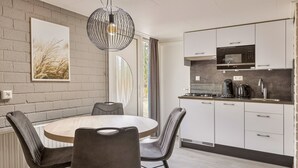 A modern kitchen with white cabinets, a round dining table, and a pendant light. - Semi-detached bungalow for 2 persons (Kootwijk)