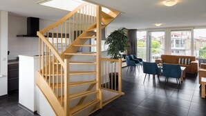 Eine moderne Wohnung mit einer Holztreppe, einer Küche, einem Wohnbereich mit Sofa und Sesseln sowie einem Balkon mit Blick.