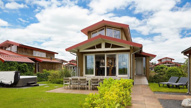 Ein modernes Haus mit Terrasse, Gartenmöbeln und einem großen Fenster.