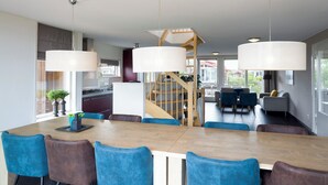Eine moderne Küche mit einer zentralen Kochinsel, einem Essbereich mit blauen Stühlen und einer Treppe, die in einen oberen Bereich führt.