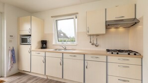 A modern kitchen with a gas stove, a microwave, a coffee maker, and a window with a view of a house.