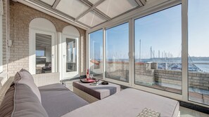 A balcony with a view of a marina, a cushioned seating area, and a glass door leading to a room.