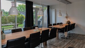 Un comedor moderno con una larga mesa de madera, sillas negras y lámparas colgantes.