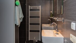 Un baño moderno con un lavabo blanco, un perchero con una toalla verde, un secatoallas blanco y un espejo sobre el lavabo.