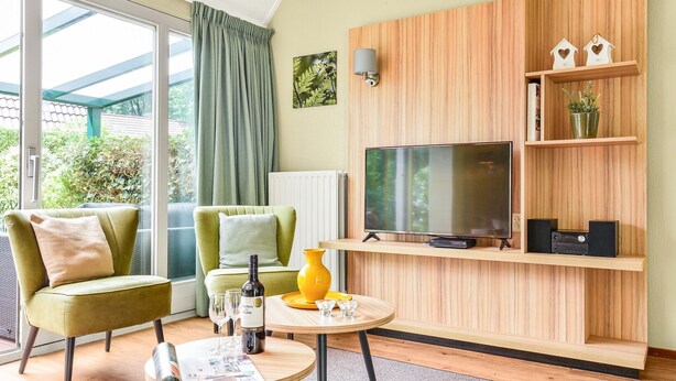 Un salon moderne avec un téléviseur, des étagères en bois et un coin repas comprenant une table et des chaises.