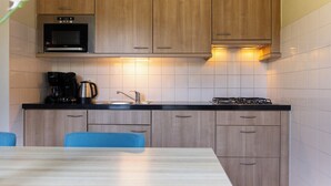Une cuisine moderne avec des meubles en bois, un plan de travail noir, un four encastré, une cuisinière à gaz, une machine à café et un évier.
