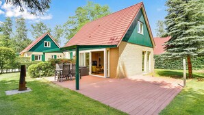 Une maison à deux étages, avec un toit recouvert de tuiles rouges, des murs extérieurs verts et un patio aménagé avec du mobilier d’extérieur.