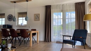 A dining area with a wooden table and chairs, a clock, and a window with curtains. - Schoonhoven Wellness 6 (Hollandscheveld)