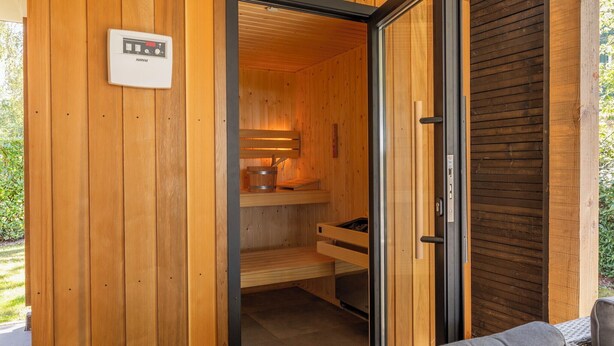 Una sauna con paredes de madera, un panel de control, un banco y un balde.