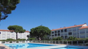 Una piscina con cerco blanco, rodeada de árboles y un edificio con techo rojo.