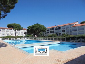 A swimming pool with a white fence, a large tree, and a building with a red roof in the background.