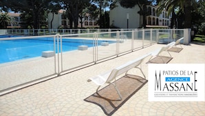 Una piscina con valla blanca, rodeada de árboles y un edificio con tejado de tejas.