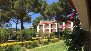 A multi-story building with a white facade and red-tiled roof, surrounded by lush greenery and flowering plants. - Renovated 3-room apartment for 6 people, close to sea (Argelès-sur-Mer)