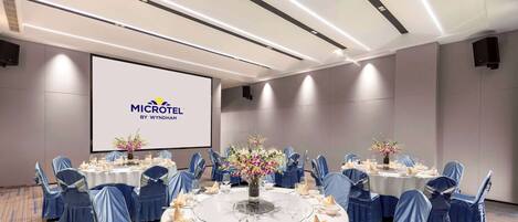 Ett konferensrum med runda bord, stolar klädda i blått tyg och en stor skärm som visar MICROTEL BY WYNDHAM-logotypen.