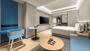 A modern hotel room with a sofa, a small round table with a tray of tea, a TV, and a blue accent wall. - Microtel by Wyndham Xishuangbanna Mengle (Xishuangbanna Dai)