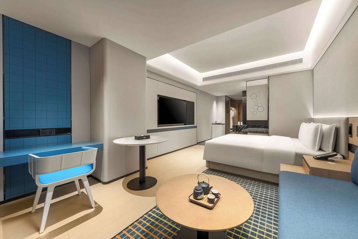A modern hotel room with a sofa, a small round table with a tray of tea, a TV, and a blue accent wall.