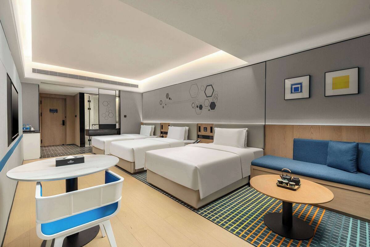 A modern hotel room with two beds, a sofa, a small table, and a TV.