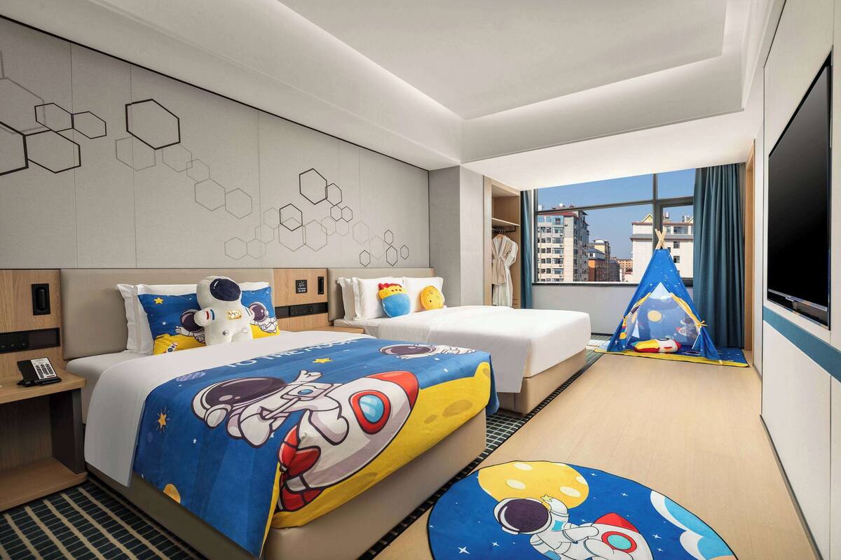 A hotel room with a large bed, a smaller bed, a TV, a wardrobe, and a window with a city view.