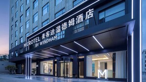 A modern hotel entrance with a revolving door, illuminated signage, and a glass facade. - Microtel by Wyndham Xishuangbanna Mengle (Xishuangbanna Dai)