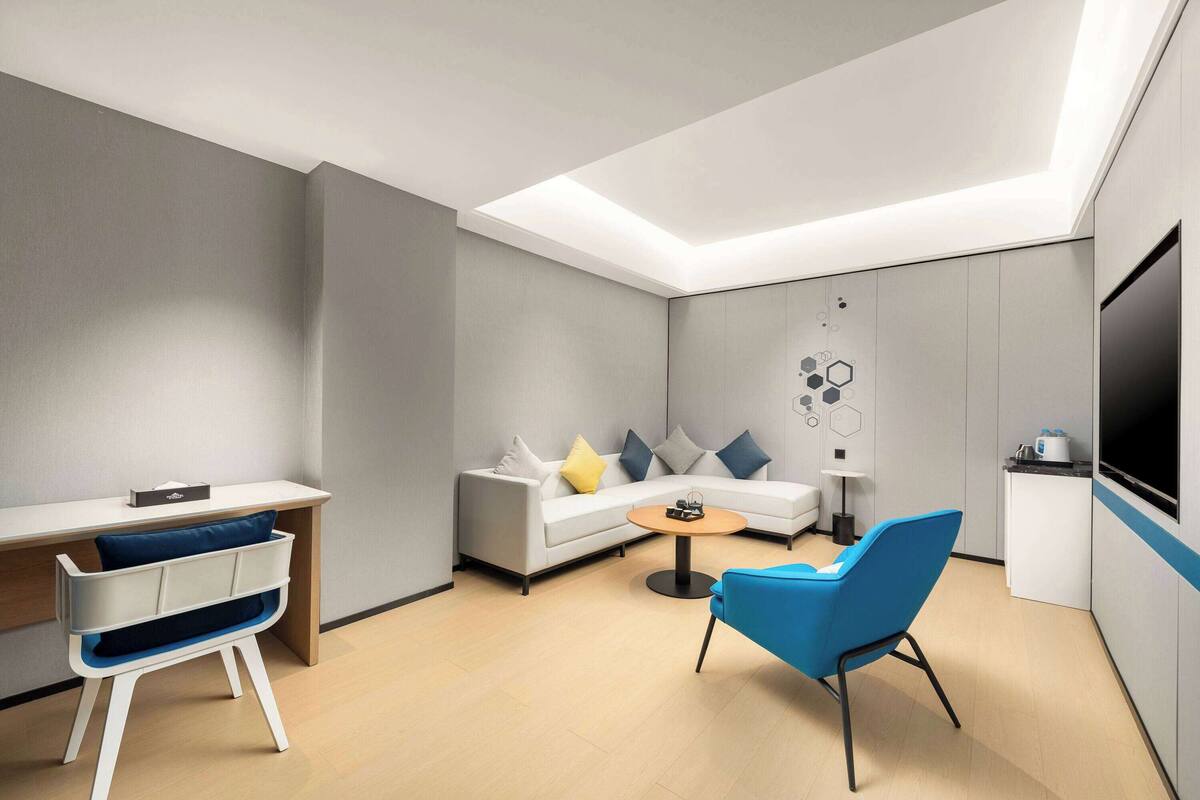 A modern, compact living space with a sofa, a blue chair, a small round table, and a TV mounted on the wall.