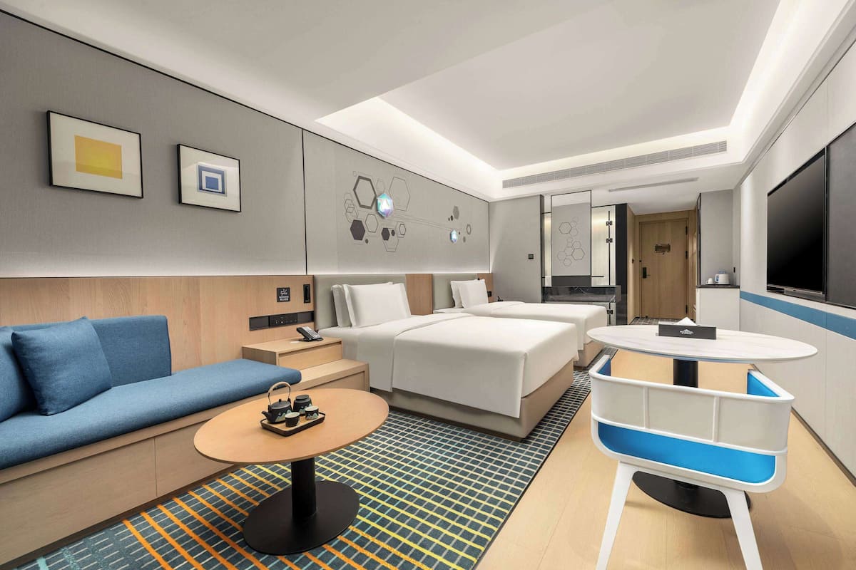 A modern hotel room with a sofa, a bed, a round table, and a TV.