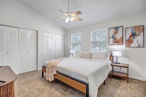 A bedroom with a bed, bedside tables, a ceiling fan, and artwork on the walls. - Spacious Downtown Historic Springfield Condo  (Jacksonville)
