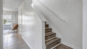 Una escalera con escalones de madera y paredes blancas que lleva a una puerta con un ventanal.