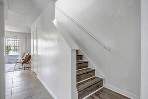 A staircase with wooden steps and white walls, leading to a door with a window. - Spacious Downtown Historic Springfield Condo  (Jacksonville)