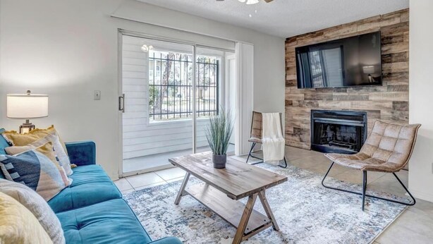Una sala de estar con sofá azul, una mesa de centro de madera, chimenea y ventilador de techo.
