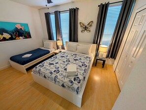 A bedroom with a bed, two bedside tables, a nightstand, a painting, and a window with curtains. - 4846-Epic 3-Suite Townhome at Vista Cay (Orlando)