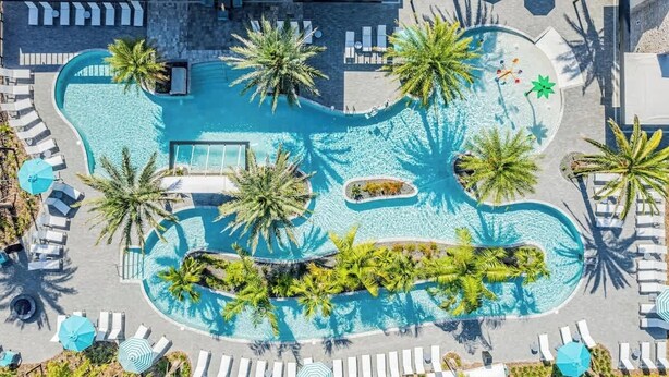Vue aérienne d’un complexe hôtelier doté d’une grande piscine, entourée de palmiers et de chaises longues.