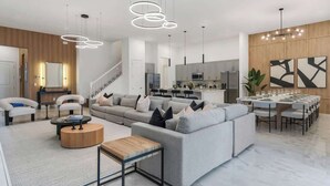 Un salon moderne avec un canapé d’angle gris, une table basse et un coin repas comprenant une longue table et des chaises.