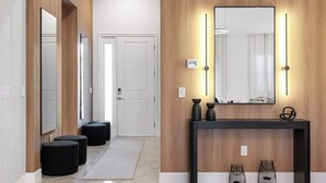 Un couloir moderne avec un lambris en bois, une console noire agrémentée d’objets décoratifs et un grand miroir avec des appliques murales.