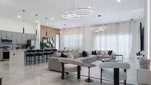 Un salon moderne avec un canapé d’angle, une table basse ronde et un coin cuisine doté de tabourets de bar.