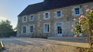 Un bâtiment en pierre de deux étages, doté de nombreuses fenêtres, une allée gravillonnée et un rosier au premier plan.