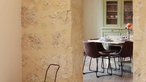 Un coin repas au style rustique, avec un mur en pierre, un plafond en bois et un meuble vert en arrière-plan.