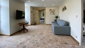 Un vaste espace de vie comprenant un téléviseur à écran plat, une table basse en bois, un canapé gris et, au fond, un coin repas.