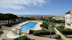 Une piscine avec vue sur la mer, entourée de verdure et de bâtiments.
