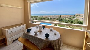Un balcon avec une table dressée pour deux personnes, offrant une vue sur la côte, avec des bâtiments et une piscine.