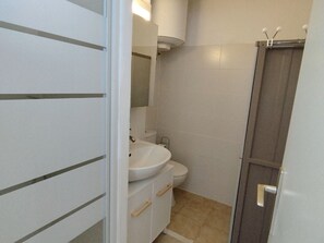 Ein kleines Badezimmer mit weißem Waschbecken, Toilette und Duschbereich.