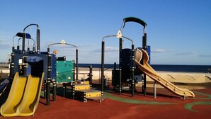 Une aire de jeux avec des toboggans et des structures d’escalade, située près d’une plage.