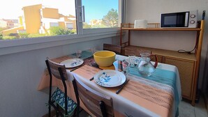 Un coin repas avec une table dressée pour deux personnes, un bol jaune, des assiettes, un pichet et un four à micro-ondes posé sur une étagère.