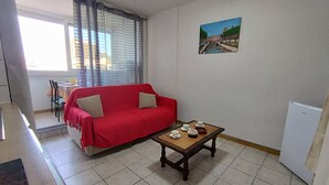 Un salon avec un canapé rouge, une table basse en bois sur laquelle sont posées des tasses et des soucoupes, un tableau accroché au mur et une fenêtre avec des rideaux.