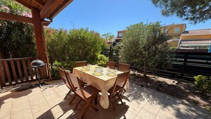 An outdoor patio with a table set for four, surrounded by wooden chairs, under a wooden pergola.