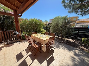 Eine Terrasse im Freien mit Tisch fĂŒr vier Personen, umgeben von HolzstĂŒhlen, unter einer Holzpergola.