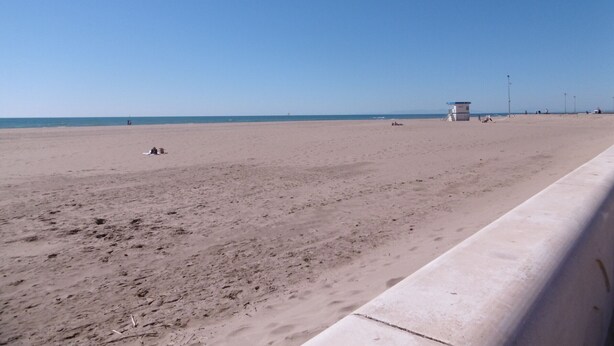 A wide sandy beach with a lifeguard tower and a concrete barrier.