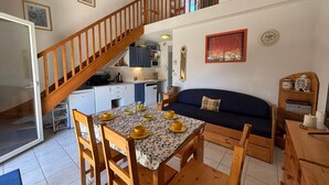 A dining area with a table set for four, a wooden staircase, a kitchen, and a living area with a sofa.