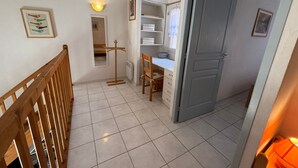 A hallway with a wooden railing, a coat rack, a chair, a desk, and a door.